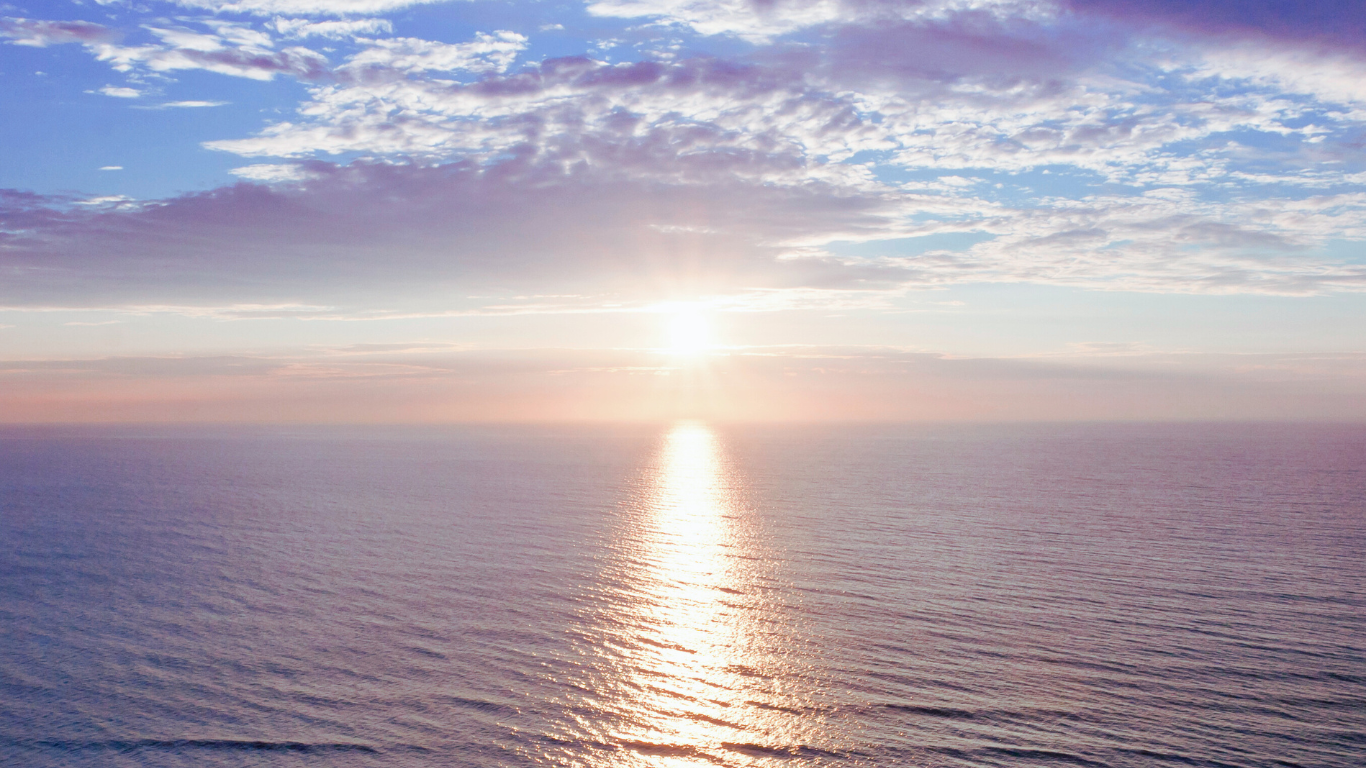 Sun rising over the ocean horizon with fluffy clouds in the sky